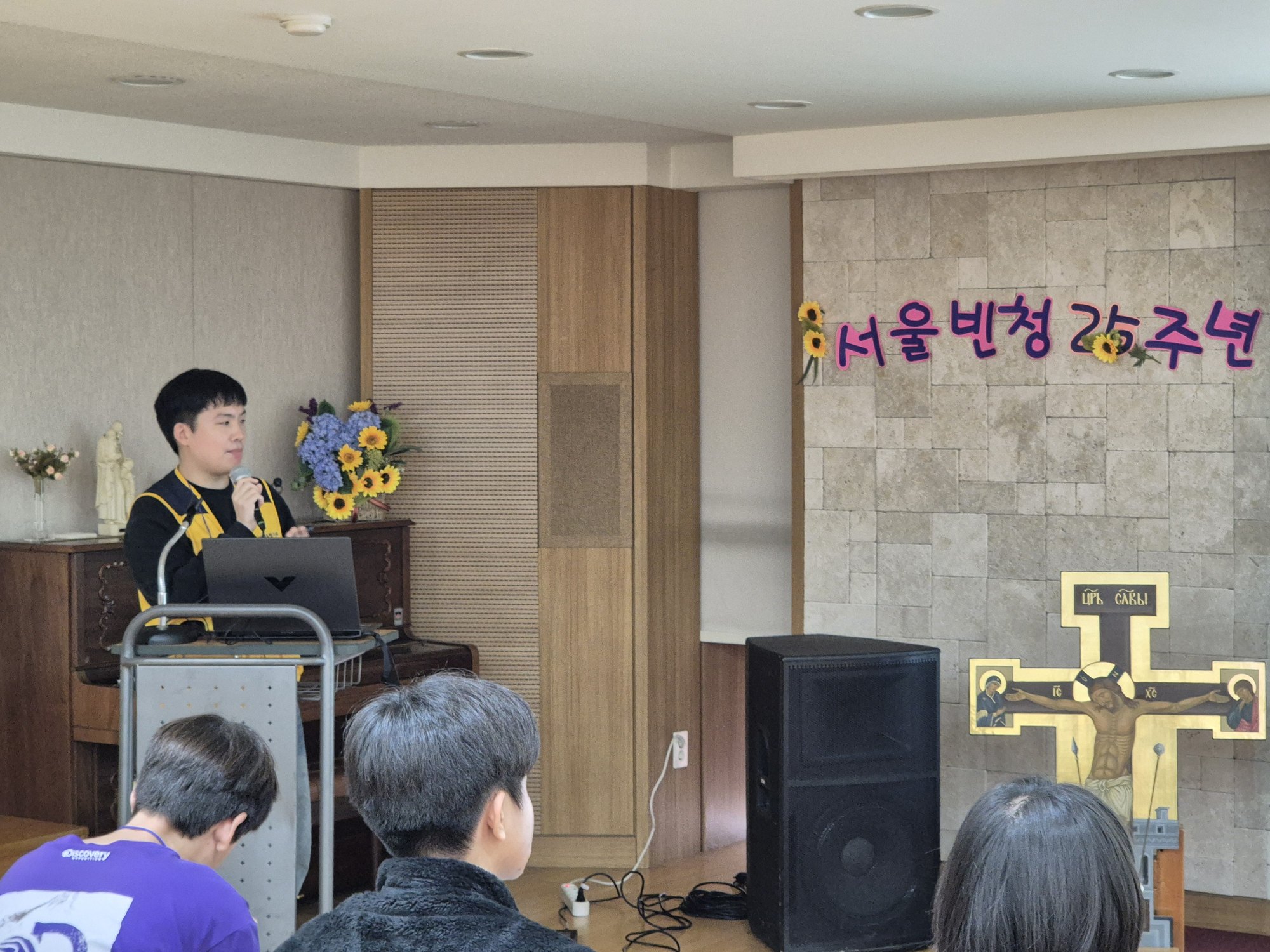 25주년 글자 벽 앞에서 발표하는 선생님