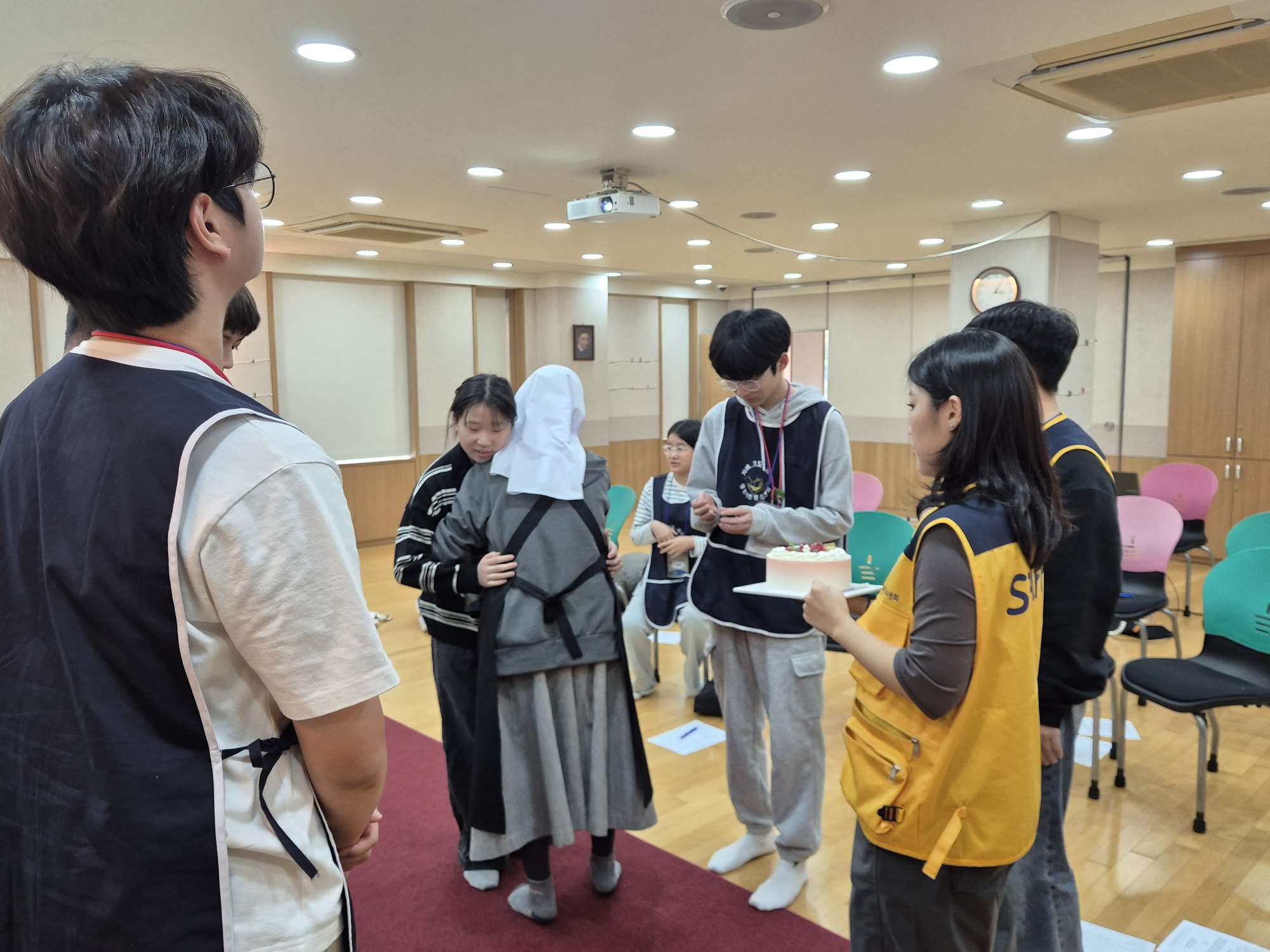 수녀님이 친구를 안아 주고 선생님이 케이크를 들고 지켜보는 모습
