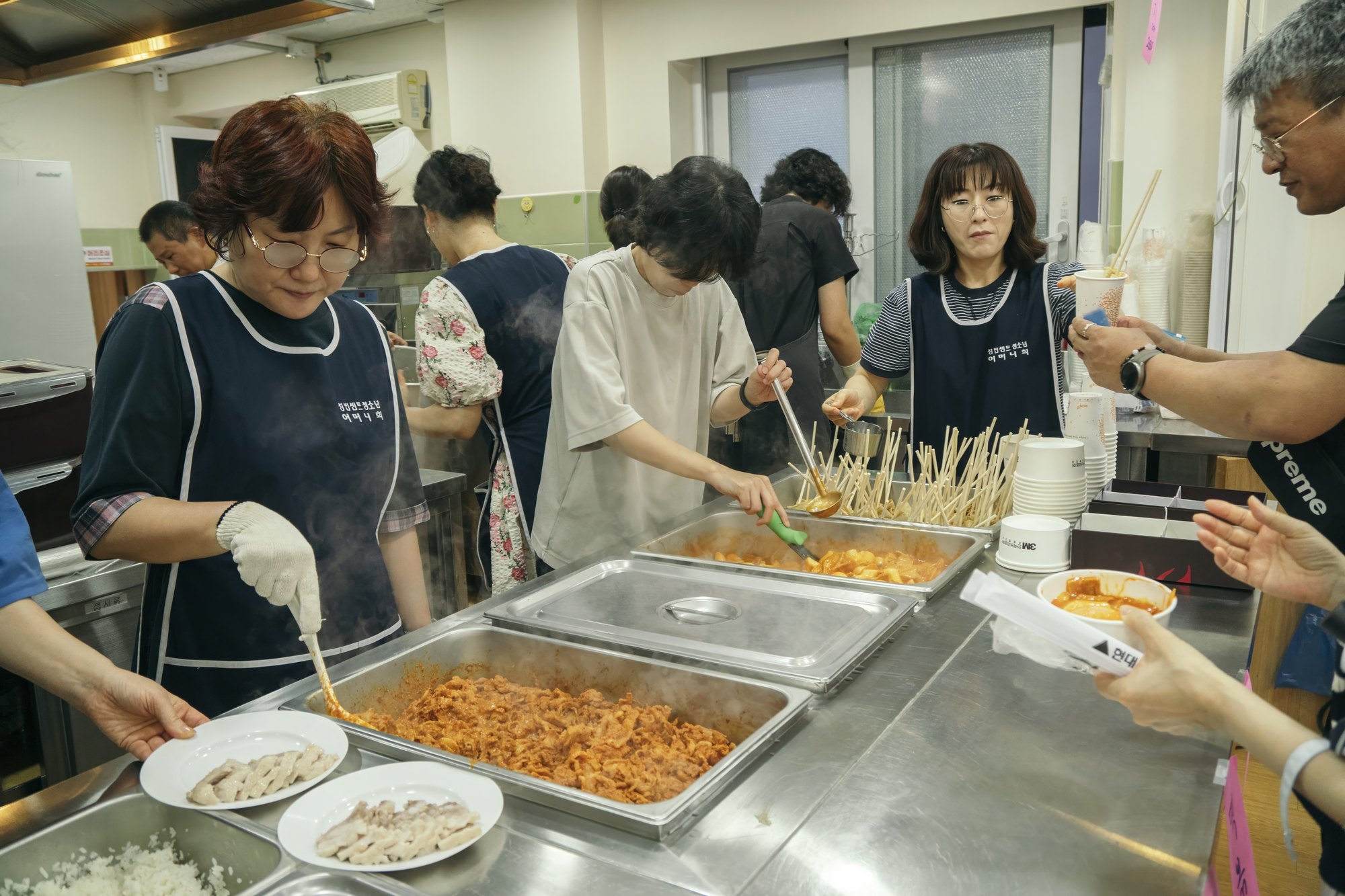 주방에서 떡볶이와 어묵을 그릇에 담아 건네는 부모님 봉사자들