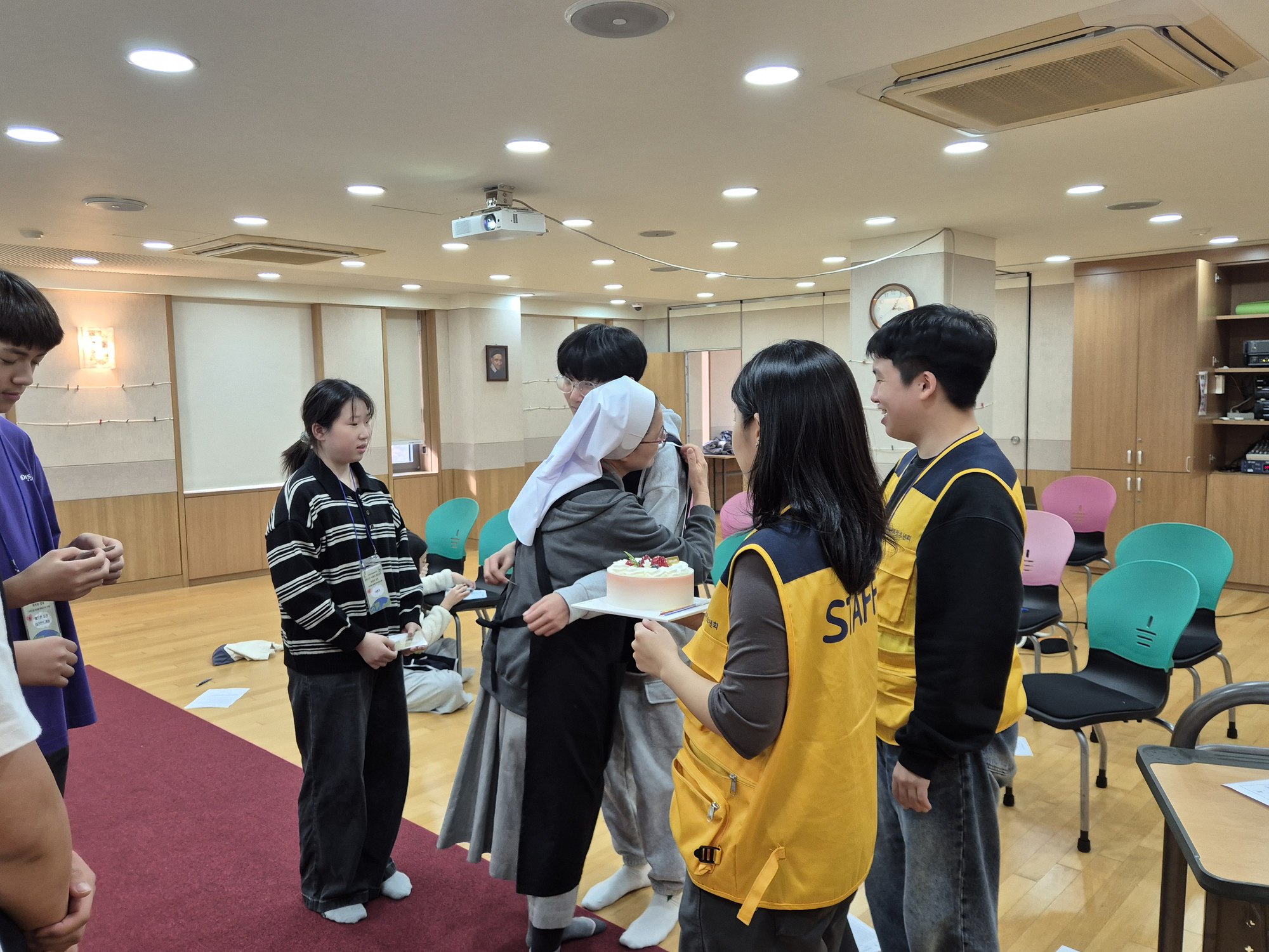 수녀님이 친구를 안아 주고 곁에서 선생님들이 웃으며 바라보는 모습