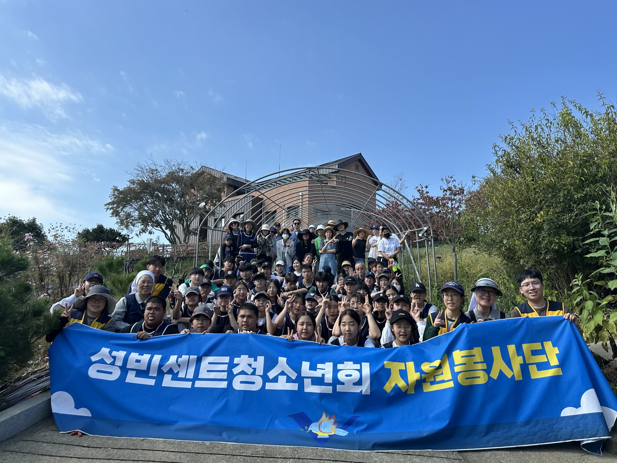 높고 파란 하늘 아래 ‘성빈센트청소년회 자원봉사단’ 현수막과 함께 찍은 단체사진