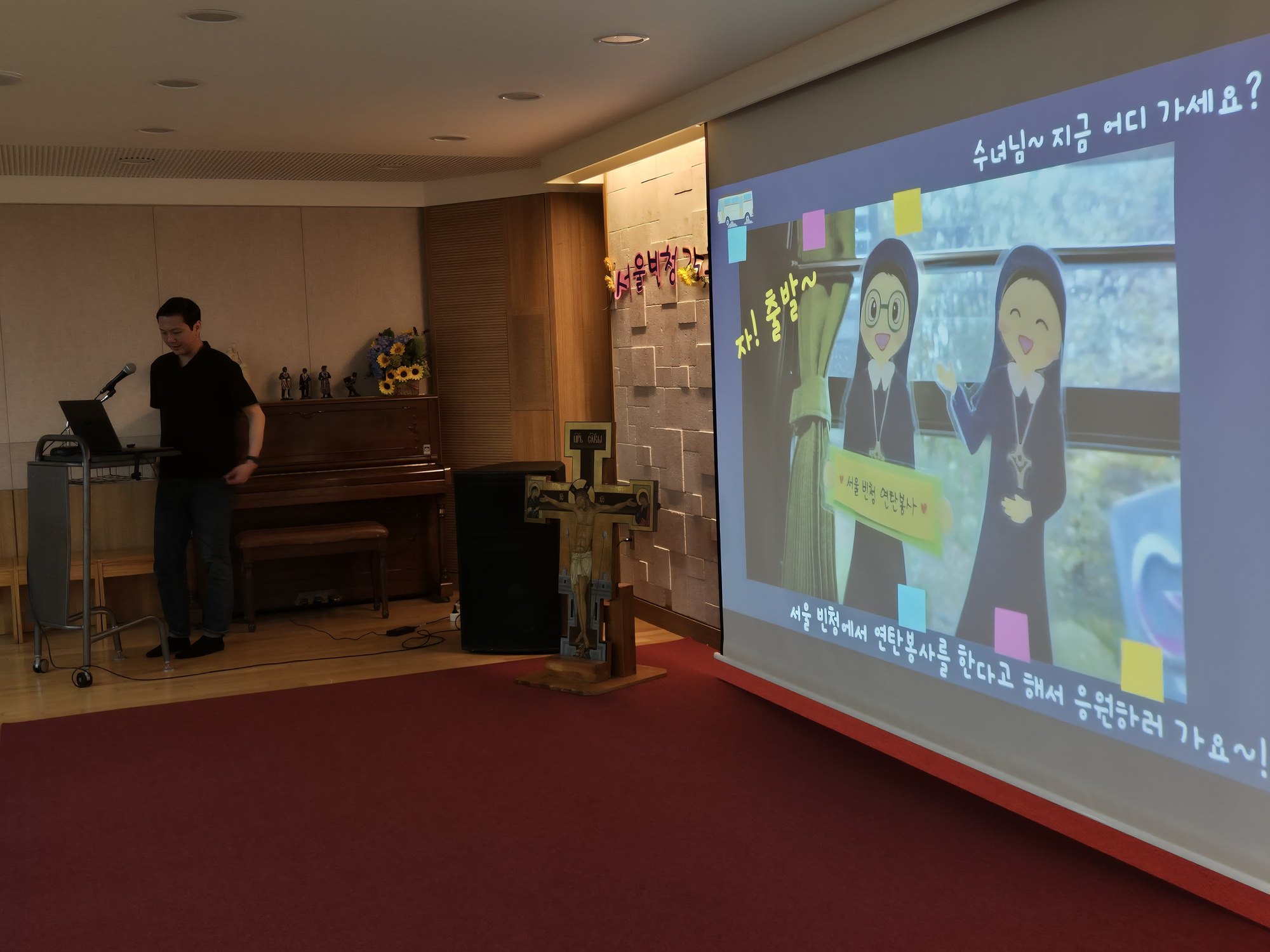 2023 연탄봉사 영상 속 수녀님 캐릭터 장면이 비치는 화면 앞의 선생님