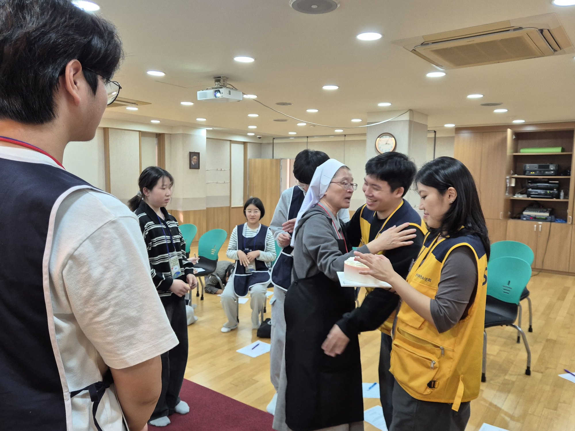 케이크를 든 선생님 곁에서 수녀님이 활짝 웃으며 선생님을 안아 주는 모습
